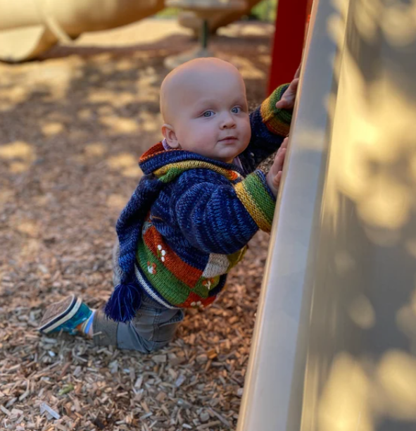 Baby in a colorful sweater climbing on playground equipment